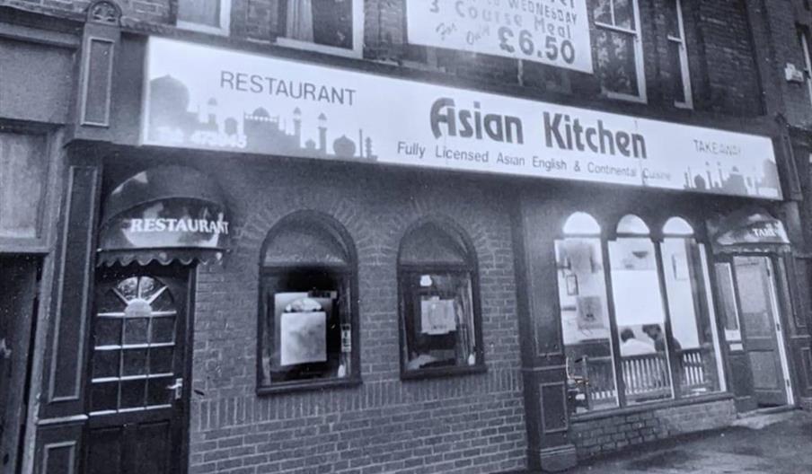 Black and white photo of a brick building with a restaurant called "Asian Kitchen." The restaurant sign advertises fully licensed Asian, English, and