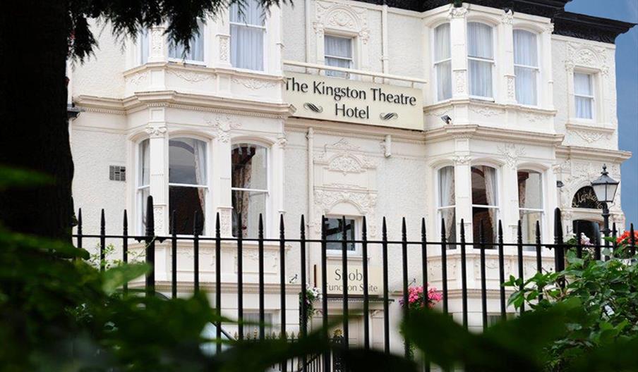 A large, ornate Victorian-style building with white stucco exterior houses The Kingston Theatre Hotel, as indicated by a prominent sign above the entr