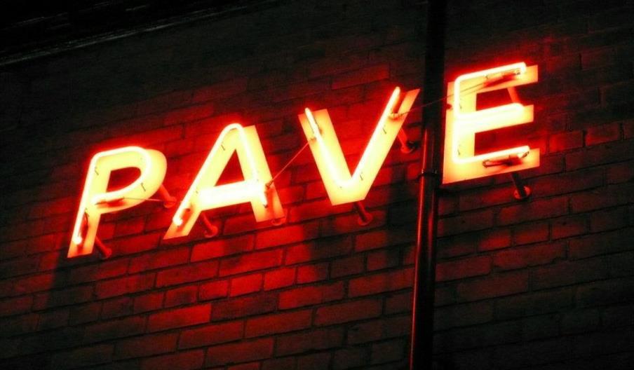 Bright red neon sign on a brick wall spelling the word "PAVE."