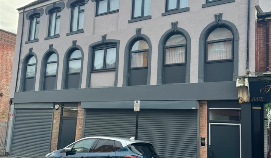 Heart of Hull Accommodation, a modern three-storey grey building in Hull city centre with arched windows and street parking outside.