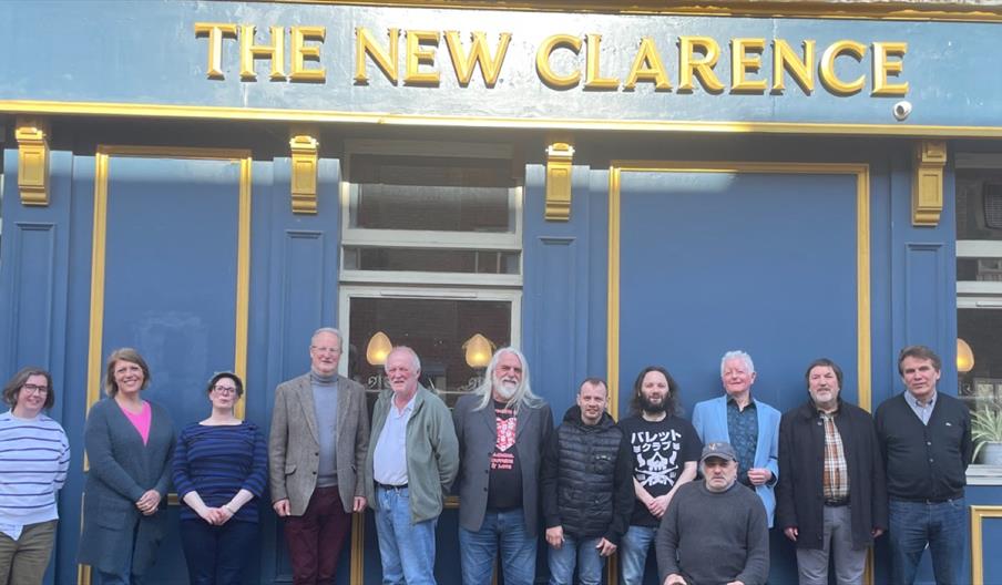 Group of people standing outside The New Clarence pub, Hull, with a blue and gold frontage and the pub name displayed above them