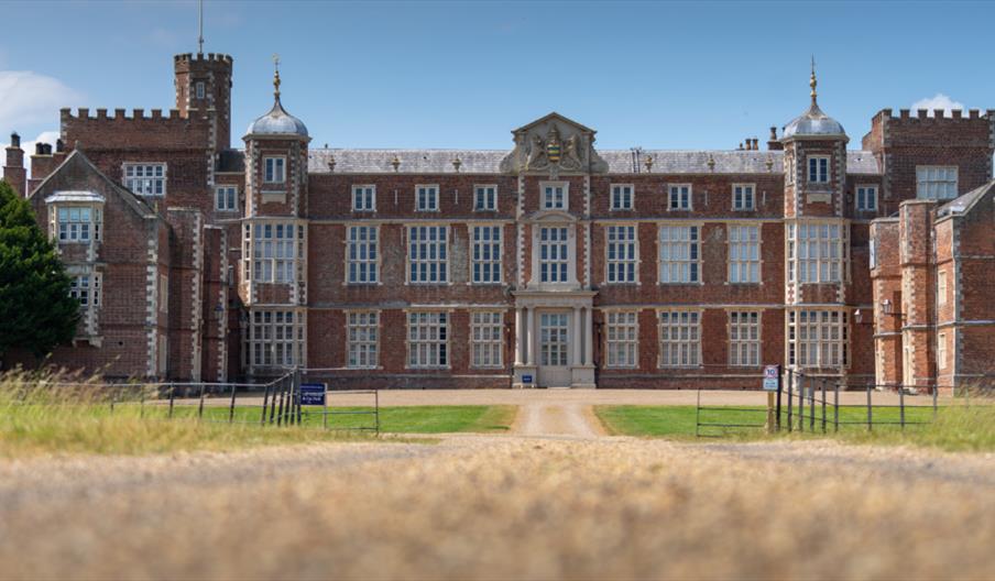 The exterior of Burton Constable Hall in Skirlaugh. It is a large stately home made of brickwork and white windows, with a view along the pathway lead