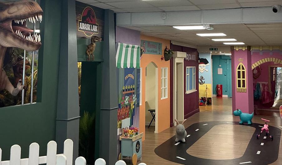 Lets play in Hull Colourful indoor play area with themed playhouses, toy animals, and a large dinosaur display.