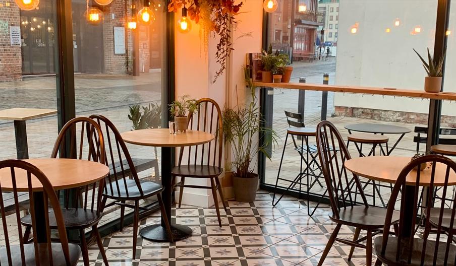Interior of Flour & Feast café in Hull Marina, featuring wooden tables and chairs, warm pendant lighting, indoor plants, patterned tiled flooring, and