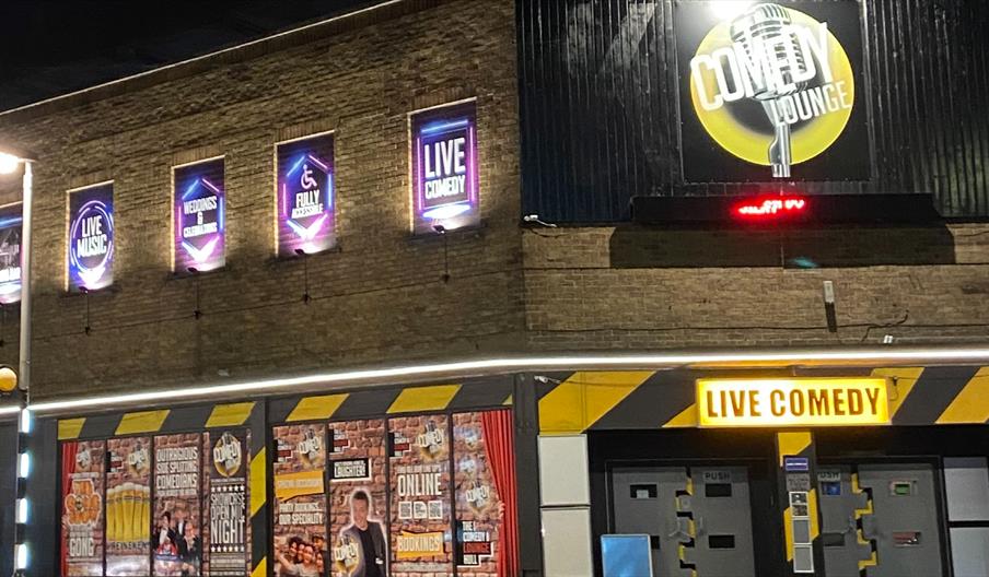 Exterior of The Comedy Lounge in Hull at night, featuring illuminated signage advertising live comedy, live music, weddings and celebrations, with bri