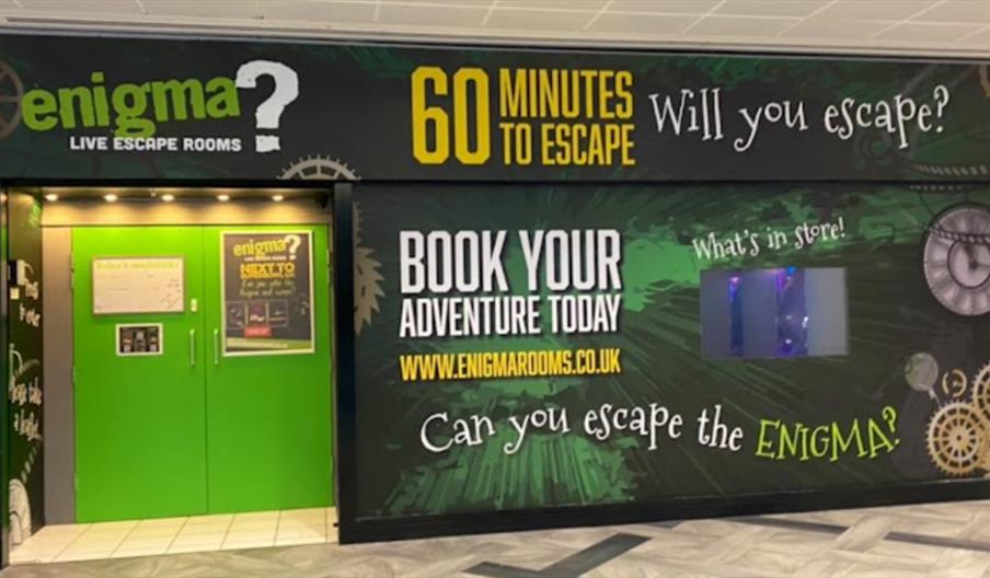 Entrance to Enigma Live Escape Rooms with bright green doors and large signage promoting “60 minutes to escape” and booking information.