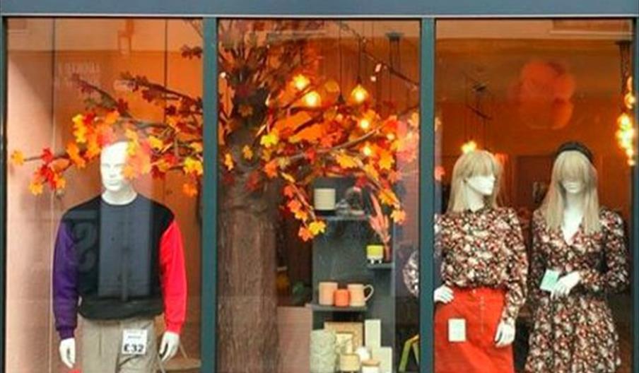 Storefront window display for "19POINT4" with three mannequins dressed in trendy autumn outfits, standing in front of a decorative tree with orange an