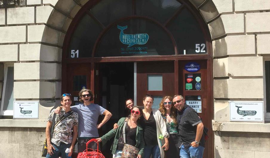 A group of travellers with luggage outside the main entrance.