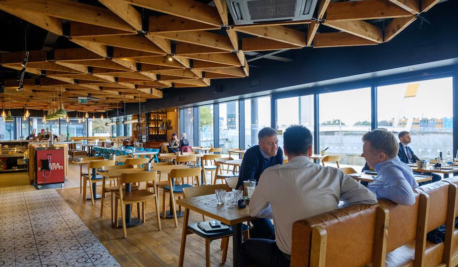 nside of restaurant, large windows with view of the River Hull, wooden tables and chairs and several groups of people eating and chatting