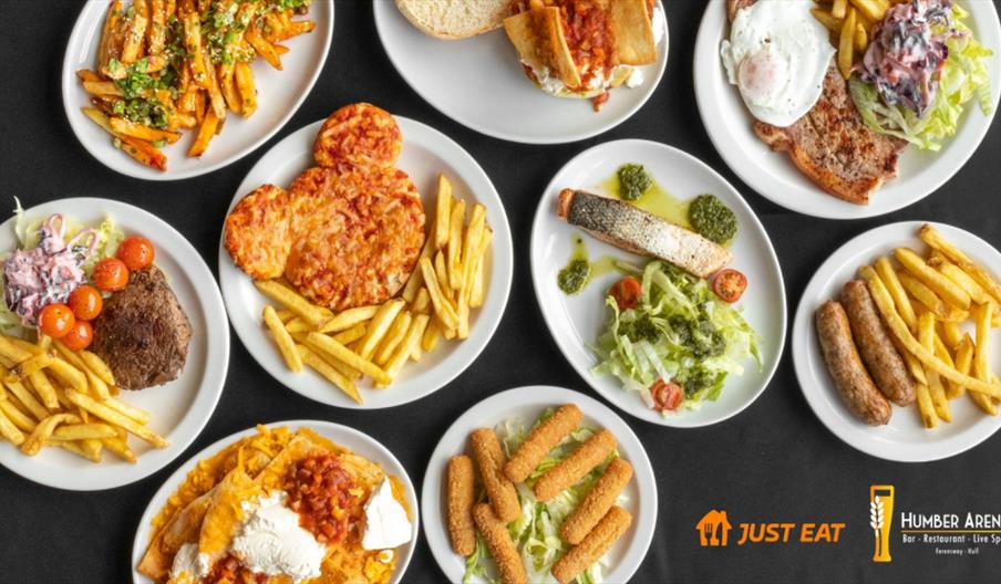 An overhead view of several plates with different meals, including fries, burgers, grilled meat, sausages, breaded cheese sticks, salad, a dish shaped