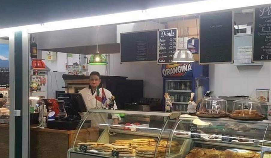 Stall with glass cabinets full with fresh, baked goods and staff member behind the cash register.