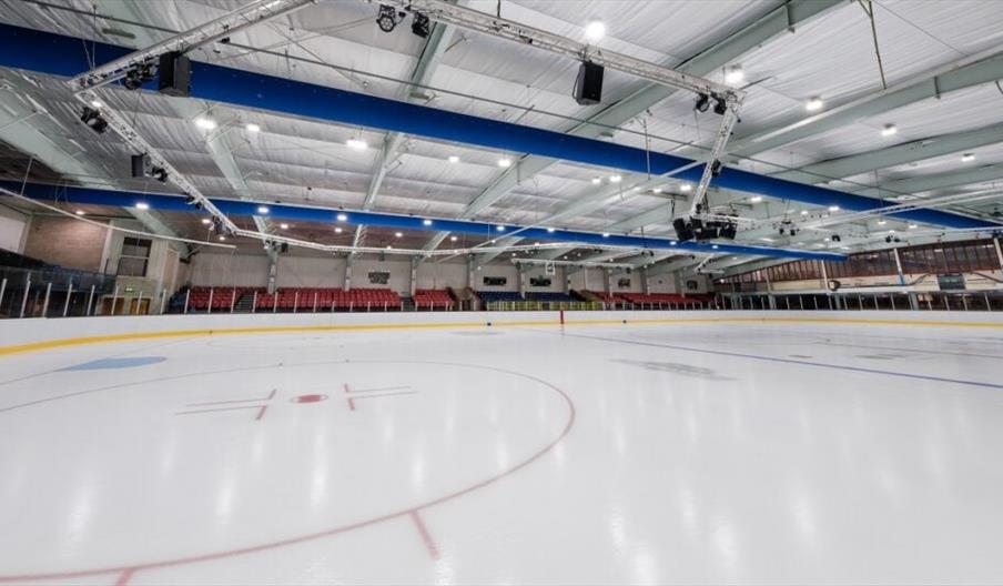 An indoor view of an Ice Rink, with a see-through barrier and a viewing area around the edges.