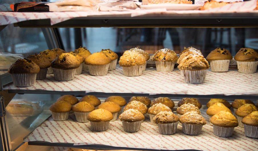 Glass  display cabinet with three shelfs and a selection of various muffins.