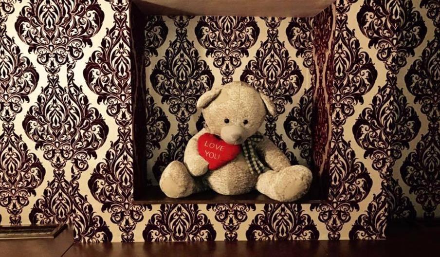 Interior of Oak Vaults. A beige teddy bear holding a red heart-shaped pillow that says "I LOVE YOU" sits in a recessed shelf with ornate brown and cre