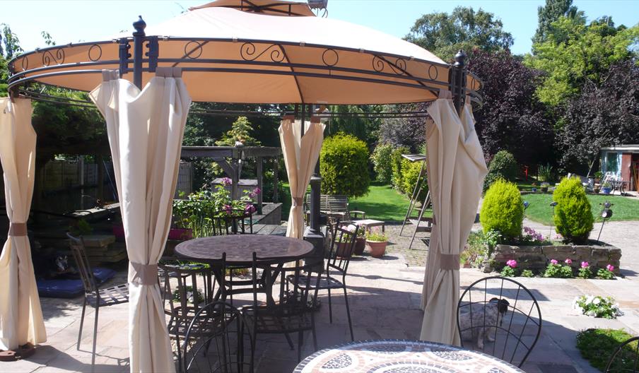 A  view of the garden in summmer with an ornamental metal gazebo, table and chairs at Acorn Guest House in Hull.