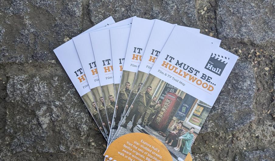Seven copies of the Hullywood Trail leaflet fanned out on a stonebrick background.