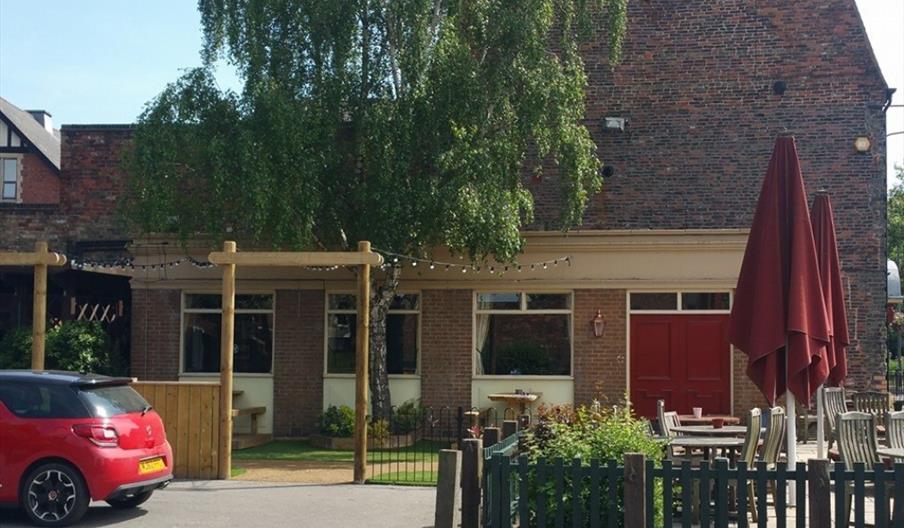 Exterior of public house with  fenced beer garden and tables with red umbrellas