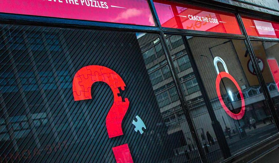 The outside windows of Escape Room Hull, showing pictures of a red question mark, padlock, and exit sign on a black background.