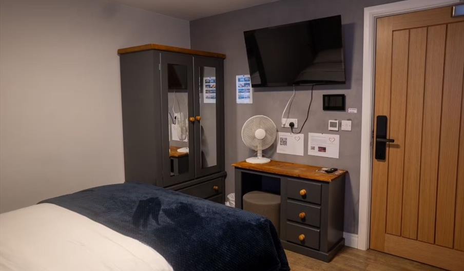 Hotel bedroom with double bed, wardrobe, desk and wall mounted TV.