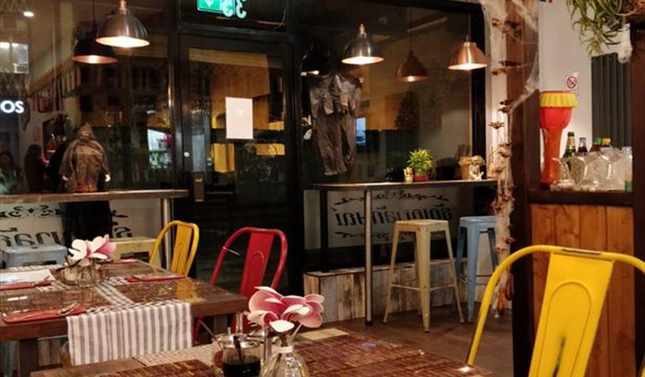 Cozy restaurant interior of Tanyalak, with wooden tables set with placemats and vases of flowers, colorful metal chairs, festive bunting and striped f