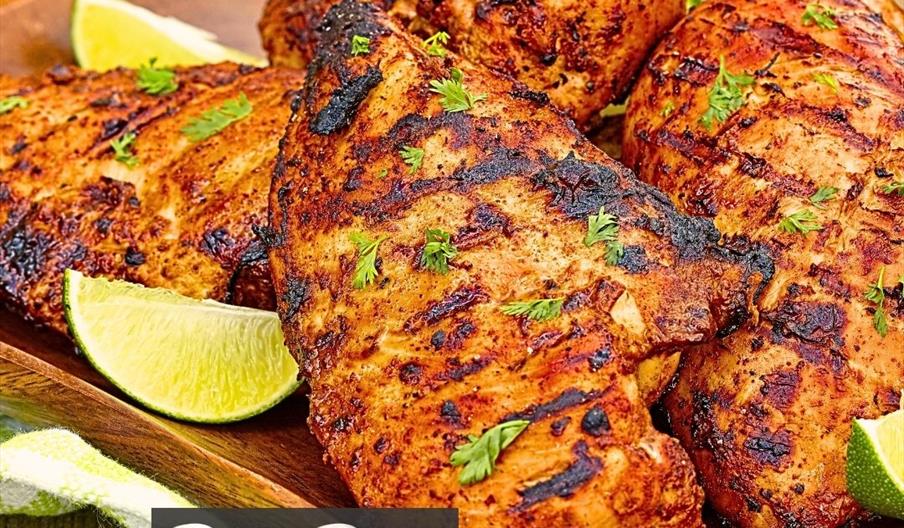 Grilled peri peri chicken breasts garnished with fresh herbs and lime wedges are arranged on a wooden platter. The image includes branding for Peri Pe