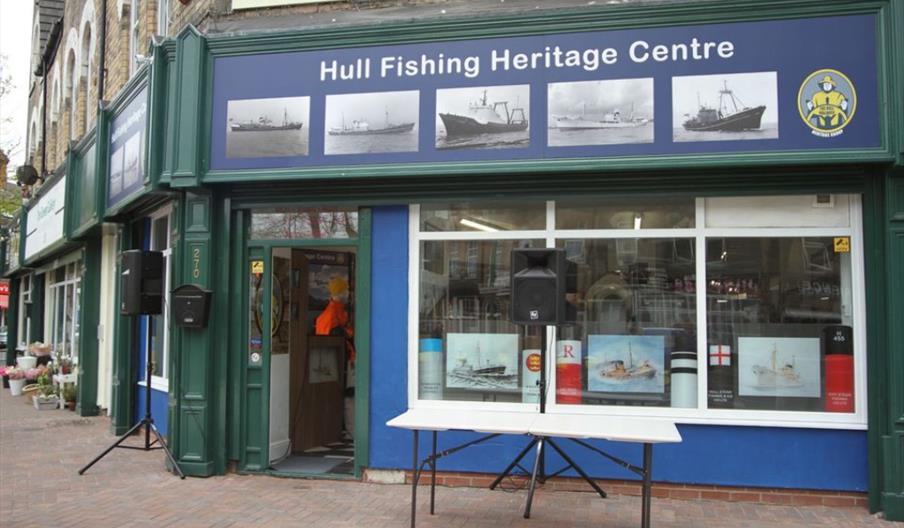 The entrance to the Heritage Centre, with a small table outside the storefront and images of fishing vessels on the sign.