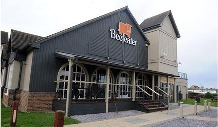 Exterior of The Kingswood. A building with a dark gray wooden facade and large windows, featuring a sign that reads "Beefeater" with an orange cow log