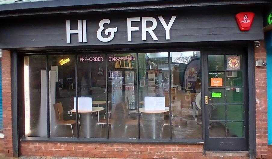 Street view of "HI & FRY" takeaway, with large glass windows showing tables and chairs inside; there is a water bowl on the pavement outside the entra