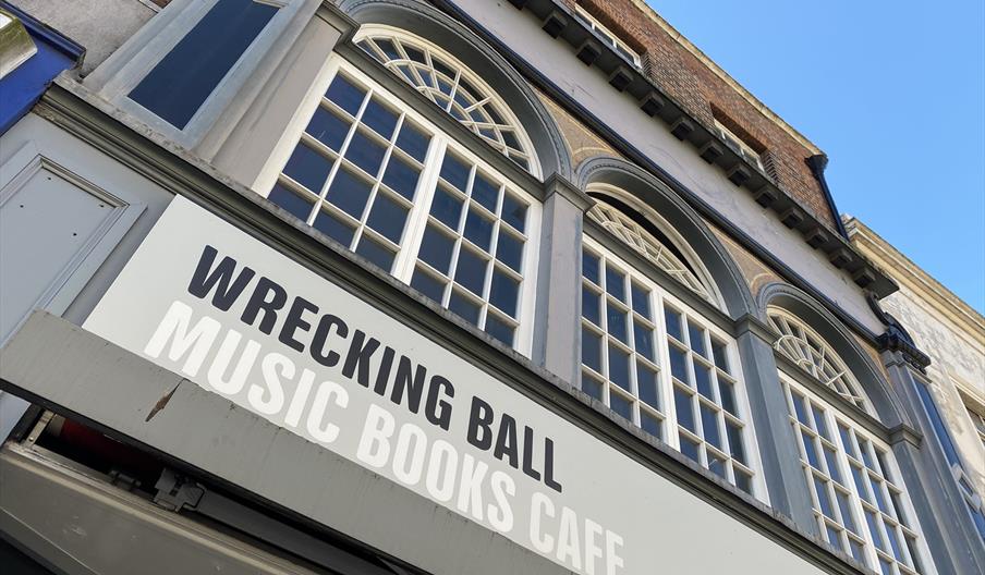 The top of a brick building with multiple large windows and the top of the storefront with a sign that reads 'Wrecking Ball Music Books Cafe'