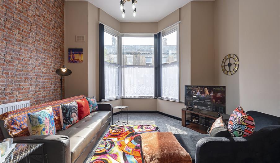 1 Stylish, colourfully decorated front room with large bay windows, two sofas and large TV