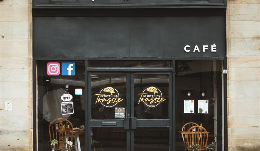 Exterior of shop with black door and windows with black trim with a white sign reading Everything Toastie.