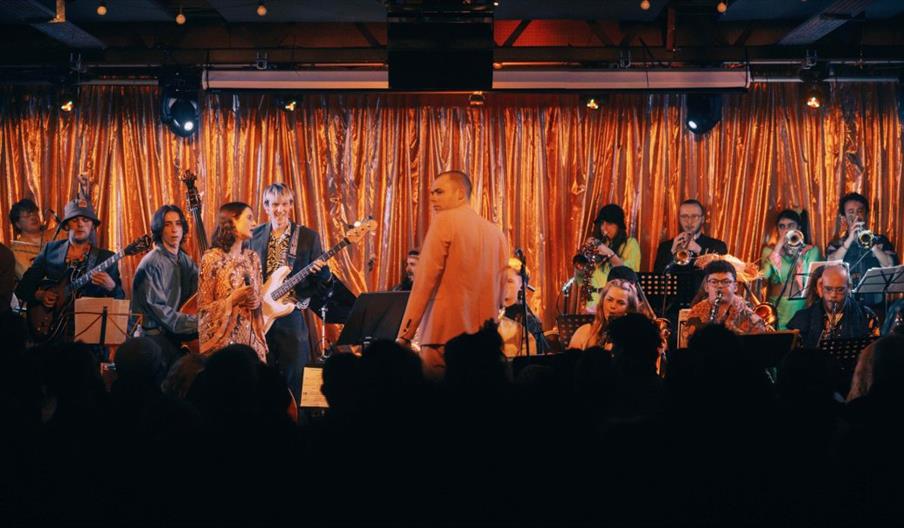 A jazz band against a metallic curtain performing to a darkened audience.