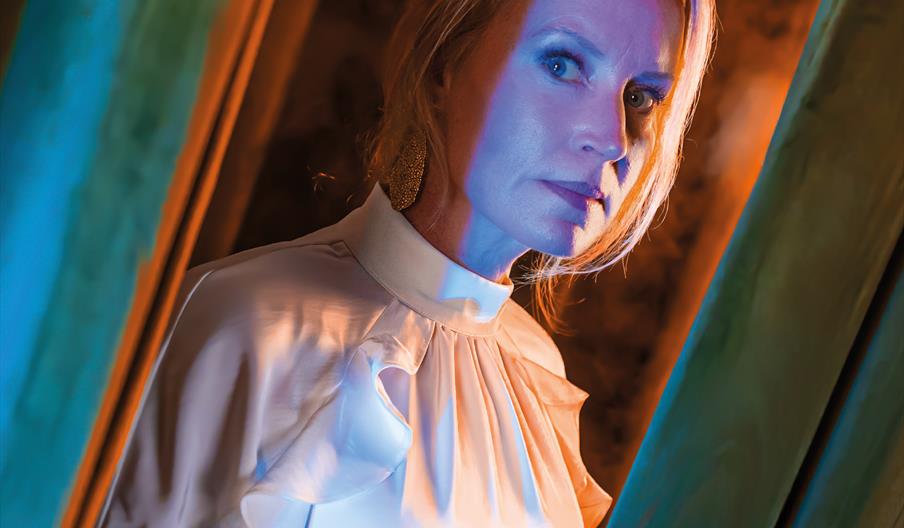 A woman in white pears around the side of a door with blue light spilling onto her face. Above the title 'Isabelle' appears in white text, with the ta
