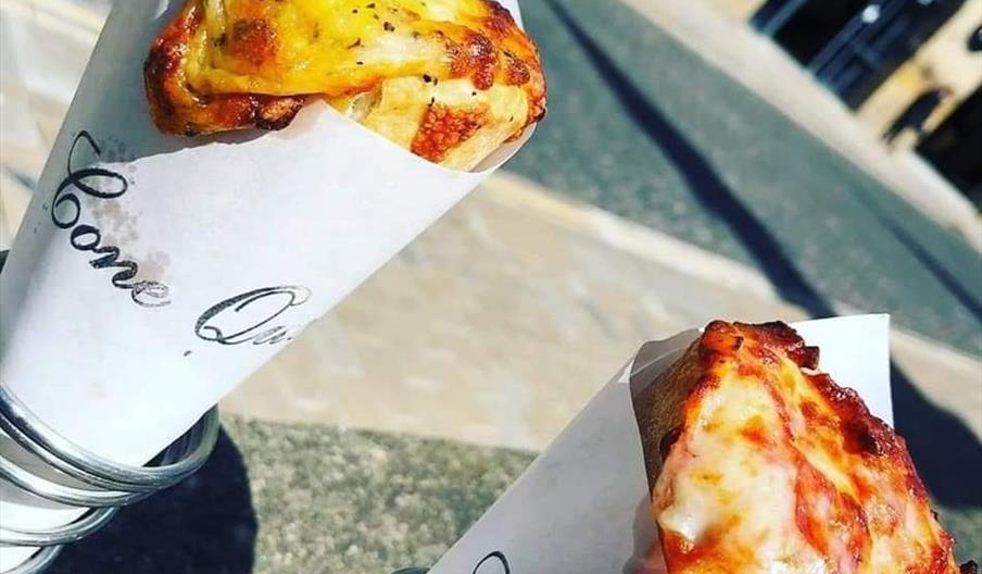 Two pizza cones, inside metal spiral holders on a wooden table outside Trinity Market.