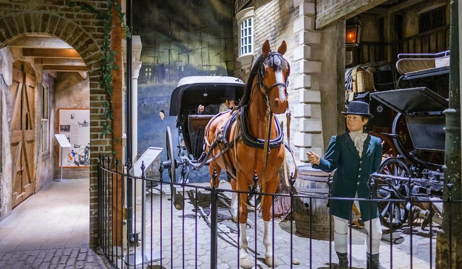 A mannequin of a man in victorian garb stands next to a horse and cart in a victorian streetscene from the Streetlife Museum.