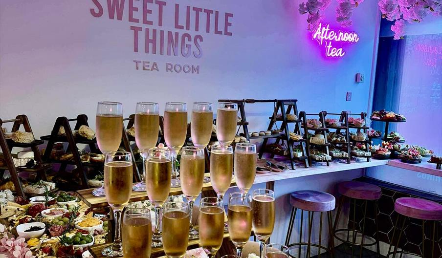 The interior of the tea room decorated with a pink floral theme features a table set with tiers of champagne glasses, various platters of finger foods