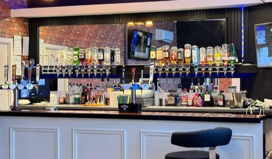 Interior of The White Hart. Two cardboard bowls on a table, each containing a savory pie with gravy, chips, and mushy peas; beside them are two glasse