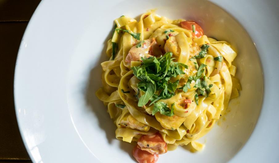 A plate of creamy fettuccine pasta topped with fresh herbs and pieces of tomato, served in a white bowl.