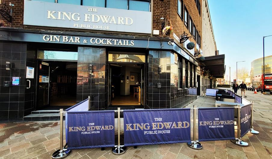 The photo shows the exterior of The King Edward Bar, a gin bar and cocktail pub with black tiled walls and large signage above the entrance. There is