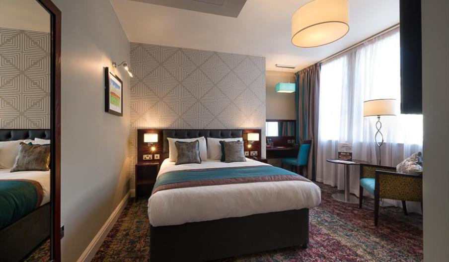 A room with a double bed, large window, mirror and blue accessories