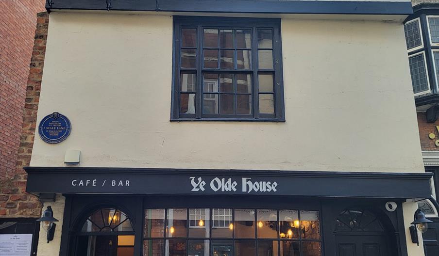 The exterior of Ye Olde House, a victorian style building with a latticed bay window, open doorway and low level lighting inside.