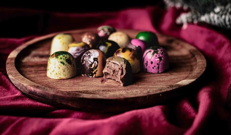 Collection of colouful chocolates on a circular, wooden board surrounded by a purple, velvet cloth.