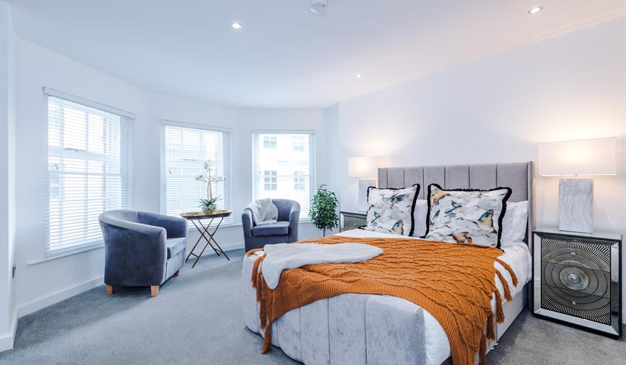 Stylish, large, bright bedroom with double bed, two grey armchairs.