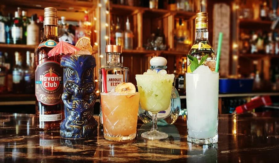 A collection of cocktails and bottles of spirits on a dark marble bar.