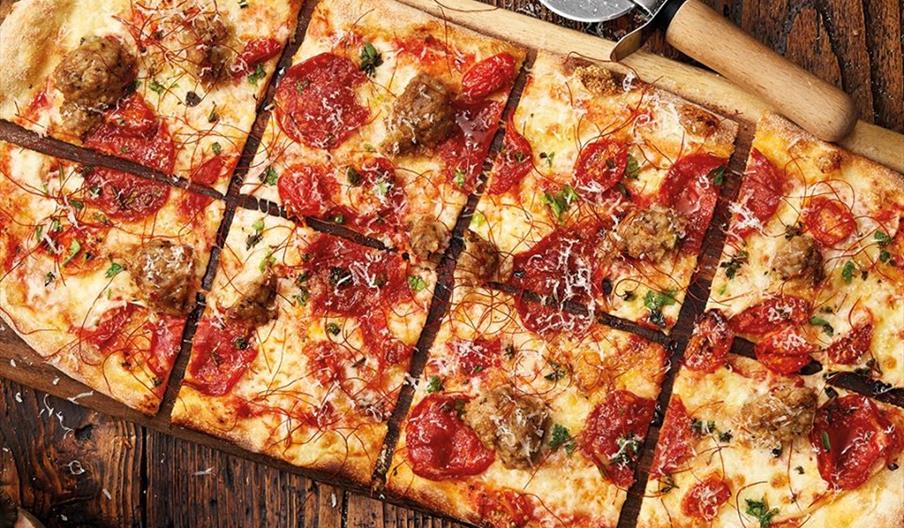 A pepperoni flatbread pizza coated in herbs and cheese on a wooden serving board with a pizza slicer next to it.