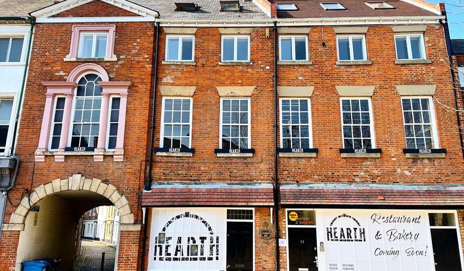 A row of historic brick buildings and an arched passageway, with large white sign in the window reading "HEARTH Restaurant & Bakery".