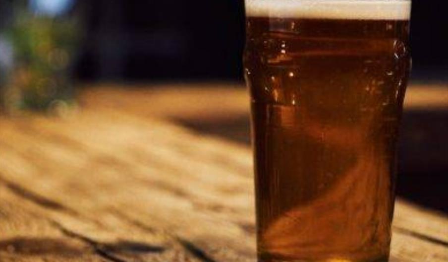 A pint of beer on a coaster on top of a rustic wooden countertop.