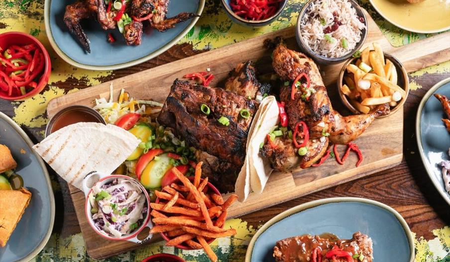 A colorful spread of grilled chicken, wings, sweet potato fries, rice, and tortillas, garnished with fresh veggies and chili.