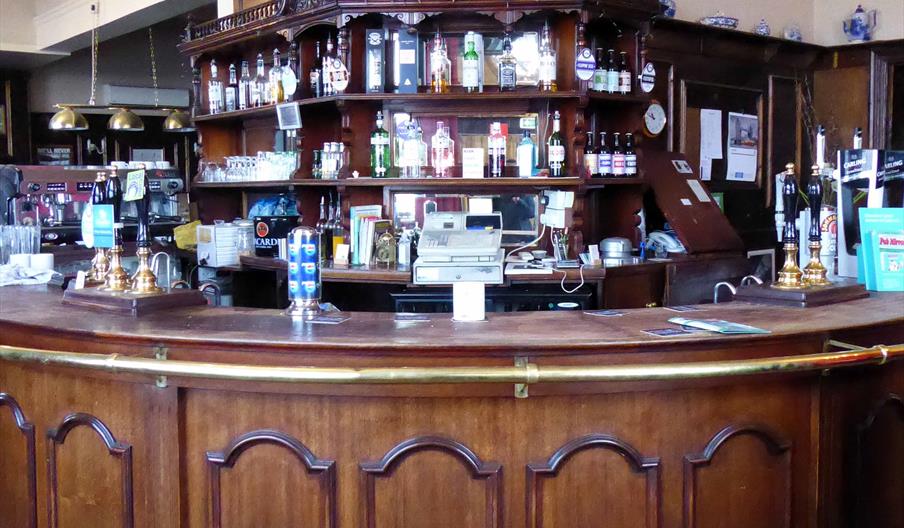 A wooden ornate bar, covered in bottles.