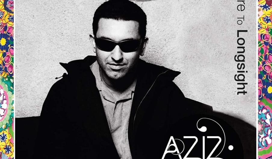 Black-and-white album cover featuring a man wearing sunglasses and a jacket, sitting with his hands folded; the background is plain with a circular de